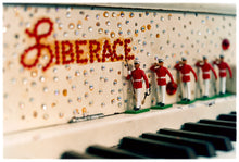 Load image into Gallery viewer, Photograph by Richard Heeps. A close up of Liberace&#39;s piano. This captures the black keys and the fall board which is decorated with crystals and red buttons spelling out Liberace in capitals. There are also 5 red and white metal soldiers positioned marching along the rim.