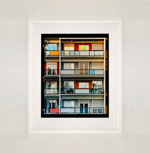 Load image into Gallery viewer, White framed photograph by Richard Heeps. This is the balconies and balcony doors of 4 floors of flats located on the Rue Dezza. The colours of the walls alternate between red and grey but look different as the light catches them.