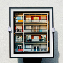 Load image into Gallery viewer, Photograph held by photographer Richard Heeps. This is the balconies and balcony doors of 4 floors of flats located on the Rue Dezza. The colours of the walls alternate between red and grey but look different as the light catches them.