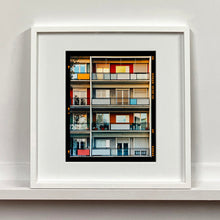Load image into Gallery viewer, White framed photograph by Richard Heeps. This is the balconies and balcony doors of 4 floors of flats located on the Rue Dezza. The colours of the walls alternate between red and grey but look different as the light catches them.White framed photograph by Richard Heeps. This is the balconies and balcony doors of 4 floors of flats located on the Rue Dezza. The colours of the walls alternate between red and grey but look different as the light catches them.