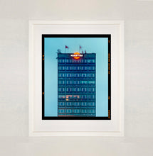 Load image into Gallery viewer, White framed photograph by Richard Heeps. High rise offices in a blue light with Martini logo on the top facade.