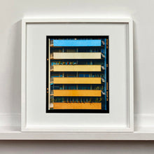 Load image into Gallery viewer, White framed photograph by Richard Heeps. Photograph of an apartment building with coloured balconies, blue at the top balcony and then fading from light yellow to a sunburnt yellow at the bottom.