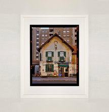 Load image into Gallery viewer, White framed photograph by Richard Heeps. A traditional Italian Tobacconist shop, here in a Swiss Cottage style building set against a vast urban apartment block.