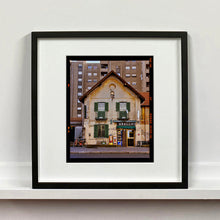 Load image into Gallery viewer, Black framed photograph by Richard Heeps. A traditional Italian Tobacconist shop, here in a Swiss Cottage style building set against a vast urban apartment block.