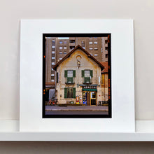 Load image into Gallery viewer, Mounted photograph by Richard Heeps. A traditional Italian Tobacconist shop, here in a Swiss Cottage style building set against a vast urban apartment block.