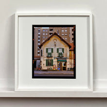 Load image into Gallery viewer, White framed photograph by Richard Heeps. A traditional Italian Tobacconist shop, here in a Swiss Cottage style building set against a vast urban apartment block.