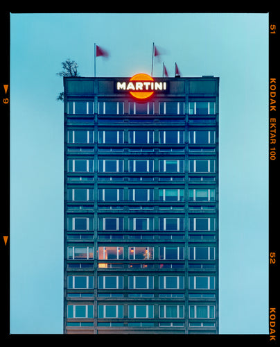 Photograph by Richard Heeps. High rise offices in a blue light with Martini logo on the top facade. 