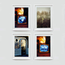 Load image into Gallery viewer, Four white framed photographs by Richard Heeps. The top left  and bottom right photographs show a black and white film, showing on a retro television, bathed in a warm light. The top right photograph shows a remote sign on a foggy fen road, the bottom left photograph is a silver trailer with a white arch entrance.