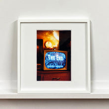 Load image into Gallery viewer, White framed photograph by Richard Heeps. A retro small brown television sits on a wooden table displaying The End on a black and white film which shows as blue and white. In the background of the television is a warm light.