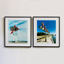 Load image into Gallery viewer, Two black framed photographs by Richard Heeps. The one on the left hand side is a roadside sign on Route 66 in America. The word ROY'S appears in a black sign with a big red arrow pointing to the left ground, below this VACANCY and on a green square the words MOTEL and CAFE. The photograph on the right hand side is a Texaco sign sitting next to a manmade waters edge.