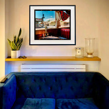 Load image into Gallery viewer, In situ photograph by Richard Heeps. Inside an American diner the light is shining on the table and the seat is the classic vibrant red faux-leather of a retro diner. The photograph is looking out of the window into the outside street.