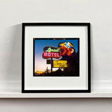 Load image into Gallery viewer, Black framed photograph by Richard Heeps. The photograph is taken in the evening, a neon sign belonging to the Lariat Motel, with a cowboy on horseback with a lasso on the right of the words, half way down the sign post is the yellow sign God Bless America.