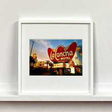 Load image into Gallery viewer, White framed photograph by Richard Heeps. This photograph is of the outside of La Concha Motel. The gold flamboyant La Concha lettering is set on a big red background. Below the motel sign is NO VACANCY with just VACANCY lit in red, below this sits a sign for Budget rent a car. Other signs and palm trees are the background together with a blue sky.