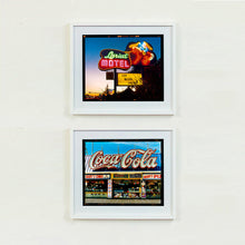 Load image into Gallery viewer, Two white framed photographs by Richard Heeps. The top photograph is taken in the evening, a neon sign belonging to the Lariat Motel, with a cowboy on horseback with a lasso on the right of the words, half way down the sign post is the yellow sign God Bless America. The bottom photograph is a row of seaside type shops with a huge Coca Cola neon sign running over the top.
