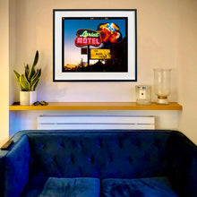 Load image into Gallery viewer, In situ framed photograph by Richard Heeps. The photograph is taken in the evening, a neon sign belonging to the Lariat Motel, with a cowboy on horseback with a lasso on the right of the words, half way down the sign post is the yellow sign God Bless America.