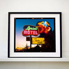 Load image into Gallery viewer, Black framed photograph by Richard Heeps. The photograph is taken in the evening, a neon sign belonging to the Lariat Motel, with a cowboy on horseback with a lasso on the right of the words, half way down the sign post is the yellow sign God Bless America.
