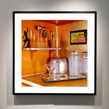 Load image into Gallery viewer, Black framed photograph by Richard Heeps. A drinks corner with martini glasses, cocktail shaker and ice bucket. There is a shelf with cocktail making equipment and it is set against retro orange walls.