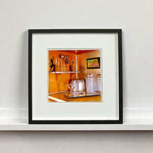 Load image into Gallery viewer, Black framed photograph by Richard Heeps. A drinks corner with martini glasses, cocktail shaker and ice bucket. There is a shelf with cocktail making equipment and it is set against retro orange walls.
