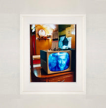 Load image into Gallery viewer, White framed photograph by Richard Heeps. A retro small brown television sits on a wooden table displaying a black and white film, with the face of Clark Gable filling the screen, it shows as blue and white. In the background of the television is a warm wood-panelled light.