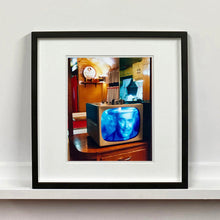 Load image into Gallery viewer, Black framed photograph by Richard Heeps. A retro small brown television sits on a wooden table displaying a black and white film, with the face of Clark Gable filling the screen, it shows as blue and white. In the background of the television is a warm wood-panelled light.