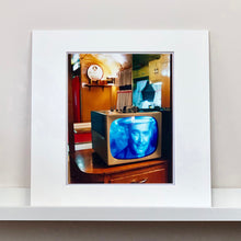 Load image into Gallery viewer, Mounted photograph by Richard Heeps. A retro small brown television sits on a wooden table displaying a black and white film, with the face of Clark Gable filling the screen, it shows as blue and white. In the background of the television is a warm wood-panelled light.