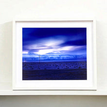 Load image into Gallery viewer, White framed photograph by Richard Heeps. A blue light hits vast land, mountains and a big sky.
