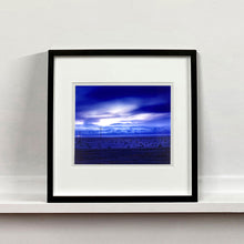 Load image into Gallery viewer, Black framed photograph by Richard Heeps. A blue light hits vast land, mountains and a big sky.
