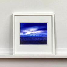 Load image into Gallery viewer, White framed photograph by Richard Heeps. A blue light hits vast land, mountains and a big sky.