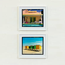 Load image into Gallery viewer, Two white framed photographs by Richard Heeps. The top photograph is of Palm Springs Pool Side and showcases classic mid-century Palm Springs California architecture. Cool blue skies and pool with accents of pink and almost neon yellow. The bottom photograph shows four beach lockers two green in the middle and two yellow on the outside on an empty beach.