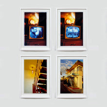 Load image into Gallery viewer, Four white framed photographs by Richard Heeps. The top two photographs show a black and white film, showing on a retro television, bathed in a warm light. The bottom two feature stairs bathed in a warm yellow light the one on the left is inside and the one on the right is outside a motel.
