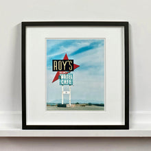 Load image into Gallery viewer, Black framed photograph by Richard Heeps. A roadside sign on Route 66 in America. The word ROY'S appears in a black sign with a bit red arrow pointing to the left ground, below this VACANCY and on a green square the words MOTEL and CAFE.