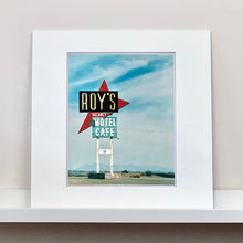 Load image into Gallery viewer, Mounted photograph by Richard Heeps. A roadside sign on Route 66 in America. The word ROY'S appears in a black sign with a big red arrow pointing to the left ground, below this VACANCY and on a green square the words MOTEL and CAFE.