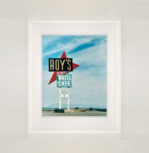 Load image into Gallery viewer, White framed photograph by Richard Heeps. A roadside sign on Route 66 in America. The word ROY'S appears in a black sign with a big red arrow pointing to the left ground, below this VACANCY and on a green square the words MOTEL and CAFE.