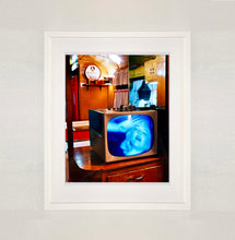 Load image into Gallery viewer, White framed photograph by Richard Heeps. A retro small brown television sits on a wooden table displaying a black and white film, with the face of Marilyn Monroe filling the screen, it shows as blue and white. In the background of the television is a warm wood-panelled light.