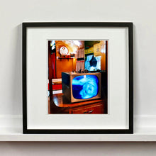 Load image into Gallery viewer, Black framed photograph by Richard Heeps. A retro small brown television sits on a wooden table displaying a black and white film, with the face of Marilyn Monroe filling the screen, it shows as blue and white. In the background of the television is a warm wood-panelled light.