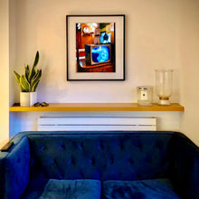 Load image into Gallery viewer, In situ black framed photograph by Richard Heeps. A retro small brown television sits on a wooden table displaying a black and white film, with the face of Marilyn Monroe filling the screen, it shows as blue and white. In the background of the television is a warm wood-panelled light.