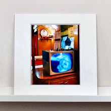 Load image into Gallery viewer, Mounted frame photograph by Richard Heeps. A retro small brown television sits on a wooden table displaying a black and white film, with the face of Marilyn Monroe filling the screen, it shows as blue and white. In the background of the television is a warm wood-panelled light.