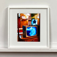 Load image into Gallery viewer, White framed photograph by Richard Heeps. A retro small brown television sits on a wooden table displaying a black and white film, with the face of Marilyn Monroe filling the screen, it shows as blue and white. In the background of the television is a warm wood-panelled light.