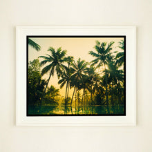 Load image into Gallery viewer, White framed photograph by Richard Heeps. Green palms trees against a warm golden sky, and reflected in a pool below.