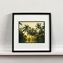 Load image into Gallery viewer, Black framed photograph by Richard Heeps. Green palms trees against a warm golden sky, and reflected in a pool below.