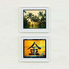 Load image into Gallery viewer, Two white framed photographs by Richard Heeps.  The top photograph is of green palms trees against a warm golden sky, and reflected in a pool below. The bottom photograph is a worn sign, worn out gold background with a Chinese character for gold painted in black.