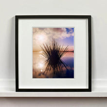 Load image into Gallery viewer, Black framed photograph by Richard Heeps. A tussock of grass sits at dusk in fenland water. It is bathed in a golden dusk light.
