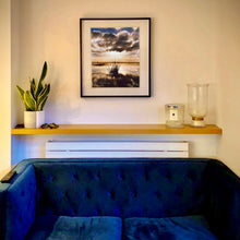 Load image into Gallery viewer, In Situ Photograph by Richard Heeps. A tussock of grass sits at dusk in fenland water. It is siting under a black and white cloud formation with a golden dusk hue.