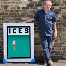 Load image into Gallery viewer, Photograph by Richard Heeps.  Richard Heeps holds a white framed print. At the top of the print, black letters spell out ICES and below is depicted a 99 icecream cone sitting left of centre against a Turquoise Teal coloured background.