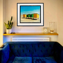 Load image into Gallery viewer, In Situ framed photograph by Richard Heeps. Yellow and green beach lockers stand on their wooden legs on the clear sandy beach.