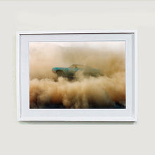 Load image into Gallery viewer, White framed photograph by Richard Heeps. A side view of a light blue Buick car moving and slightly obscured by the dust clouds which it has created.