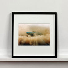 Load image into Gallery viewer, Black framed photograph by Richard Heeps. A side view of a light blue Buick car moving and slightly obscured by the dust clouds which it has created.