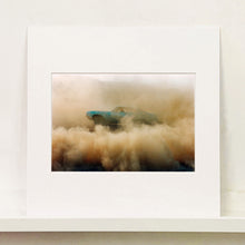 Load image into Gallery viewer, Mounted photograph by Richard Heeps. A side view of a light blue Buick car moving and slightly obscured by the dust clouds which it has created.