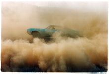Load image into Gallery viewer, Photograph by Richard Heeps. A side view of a light blue Buick car moving and slightly obscured by the dust clouds which it has created.