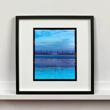 Load image into Gallery viewer, Black framed photograph by Richard Heeps. The blue bay at Llandudno, cut across the middle with path and railings with a gap right in the middle.